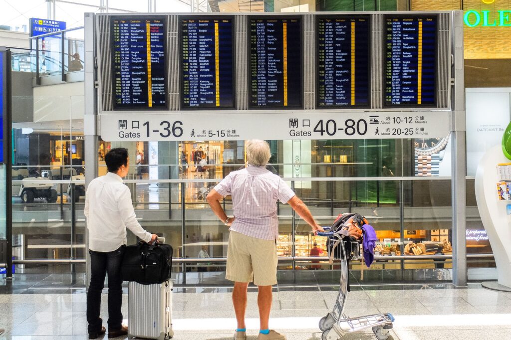 Passengers review flight information on a digital board in Hong Kong airport terminal
