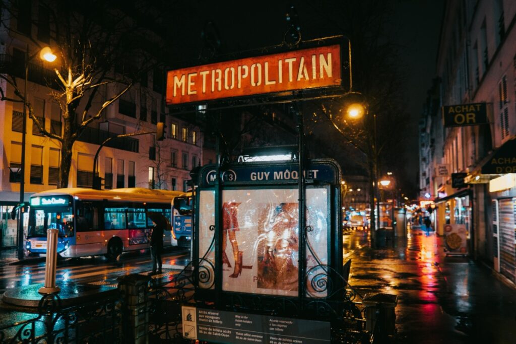 A wet Paris street captures the glow of city lights by the Metropolitain entrance at Guy Môquet metro station